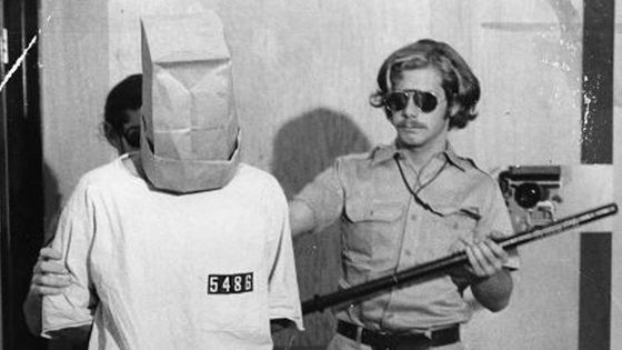 Un prisonnier se tient à côté du gardien John Loftus durant l'expérience, 1971